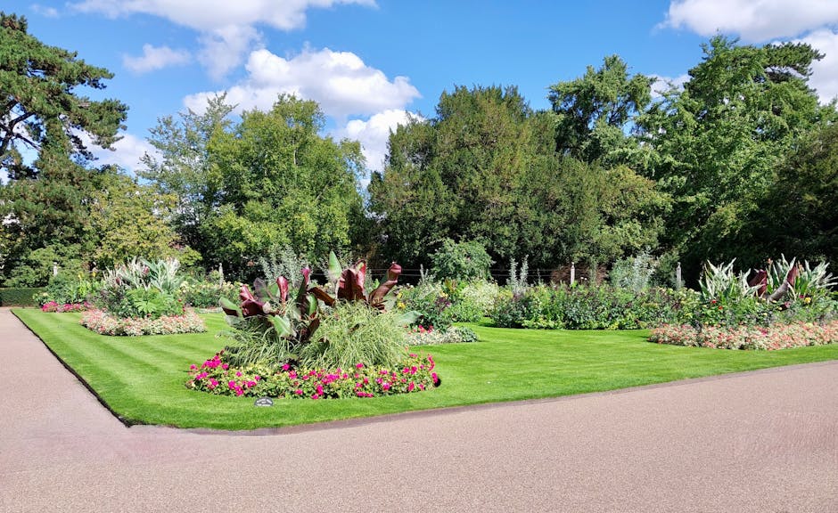 A traditional red brick house with a steep, tiled roof and multiple white-framed windows, set in a well-maintained garden. The garden features a neatly trimmed hedge bordering a lush green lawn, with